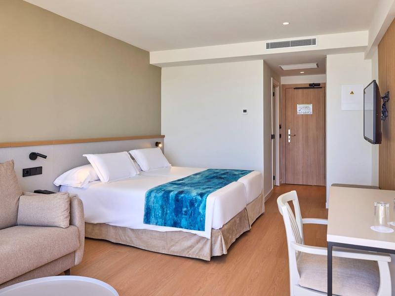 Jasno urządzone pokoje hotelowe z podwójnym łóżkiem, niebieskim narzutem i drewnianą podłogą.