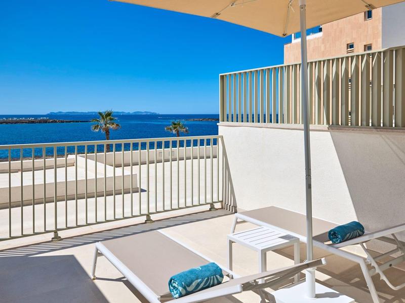 Taras z białymi leżakami i widokiem na błękitne morze pod jasnym niebem.