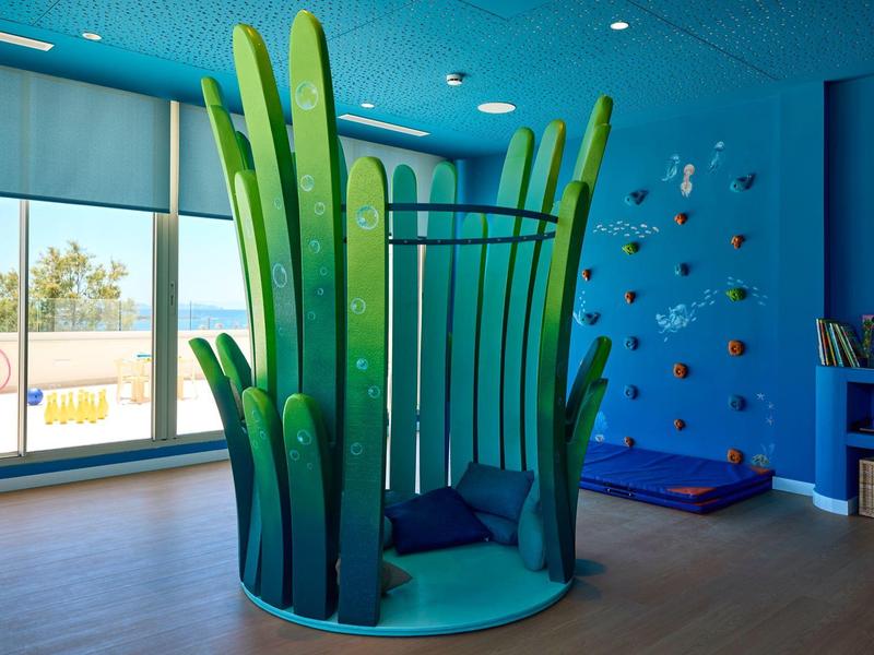 Pokój zabaw z zieloną, w kształcie rośliny, strukturą do wspinaczki i kolorowymi dekoracjami ściennymi w hotelu