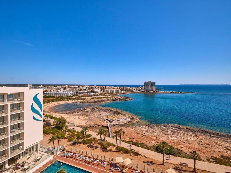 Linia brzegowa z czystą, niebieską wodą, budynek hotelu i basen pod błękitnym niebem.