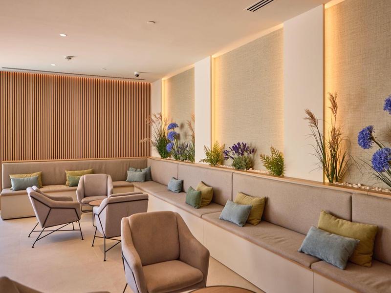 Nowoczesny, jasny salon hotelowy z wygodnymi fotelami i dekoracyjnymi roślinami przy ścianie.