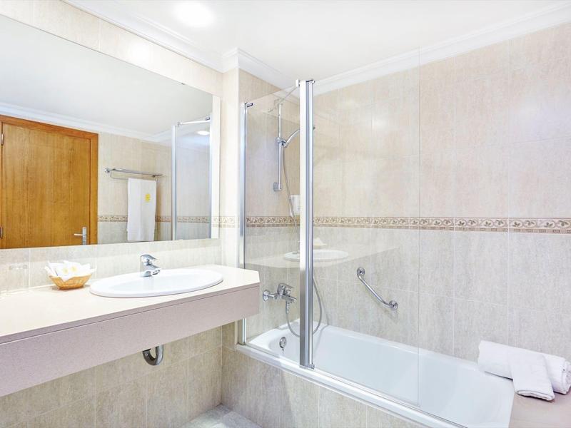 Světlá koupelna s vanou, umyvadlem, velkým zrcadlem a dřevěnými dveřmi.