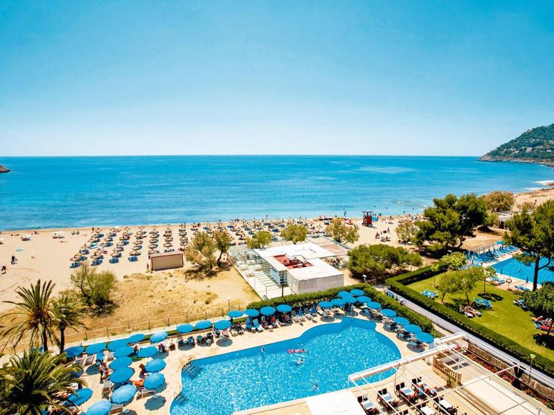 Přímořský hotel s bazény, lehátky a výhledem na modré moře za jasné oblohy.