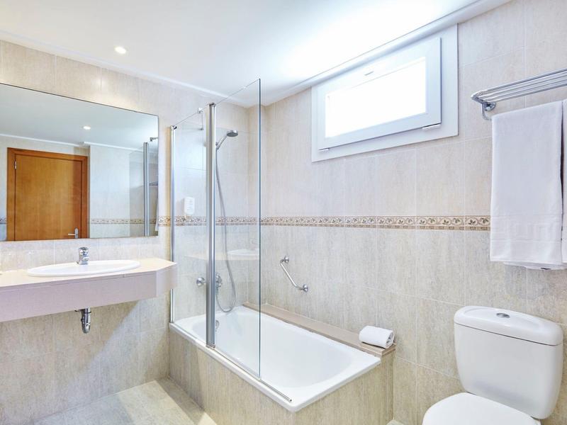 Světelná koupelna s vanou, sprchovým sklem, umyvadlem a toaletou.