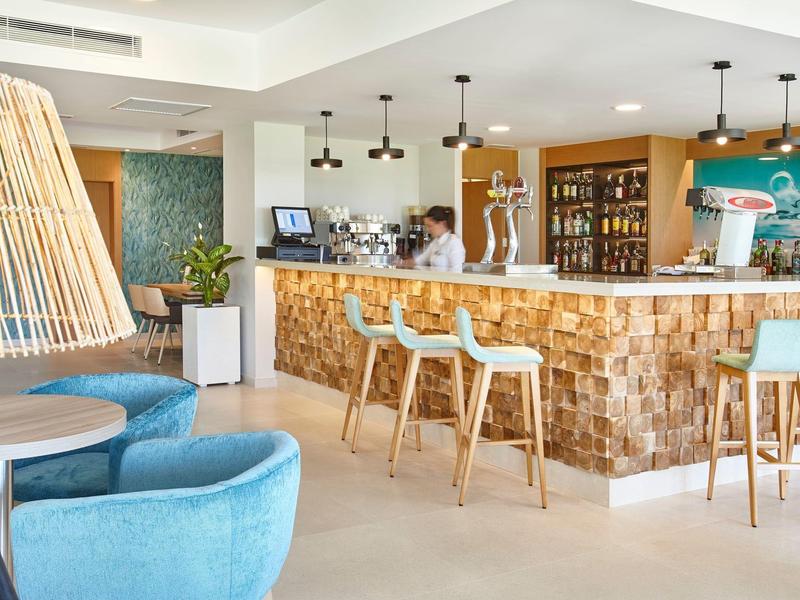 Moderně zařízený hotelový bar s dřevěným pultem a modrými křesly pod závěsnými svítidly.