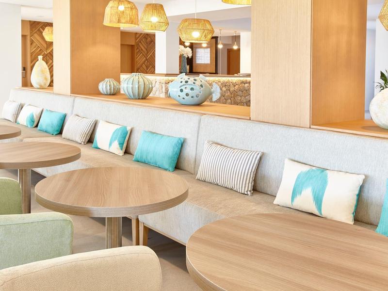 Moderní hotelový salonek s kulatými stolky, pohodlnými sedadly a dekorativními polštáři modré a bílé barvy.