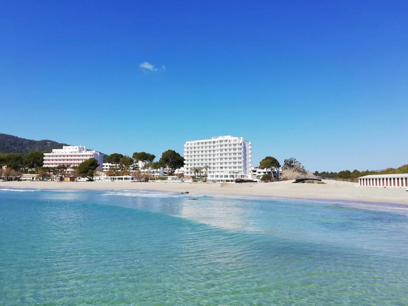 Čistá mořská voda a jasně modrá obloha nad hotelem u písečné pláže.