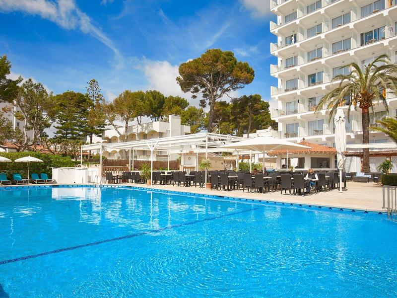 Velký hotelový bazén s lehátky a slunečníky vedle vícepodlažní budovy pod modrou oblohou.