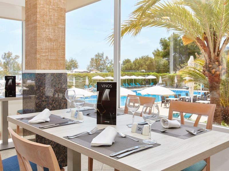 Světle zařízený stůl pro dva s výhledem na bazén a palmy v restauraci.