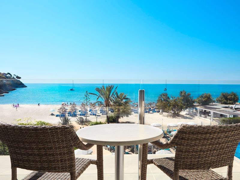 Balkon se dvěma proutěnými židlemi a stolem s výhledem na pláž a modré moře.