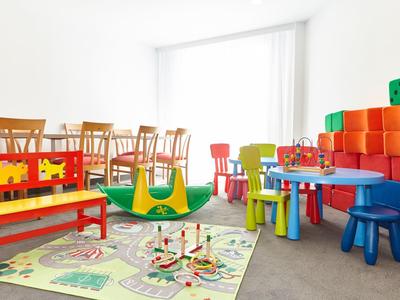 Jasny pokój zabaw dla dzieci z kolorowymi meblami i zabawkami przed dużym oknem.