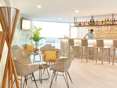 Lichte hotelbar met rotan stoelen, houten vloer en lichte inrichting.