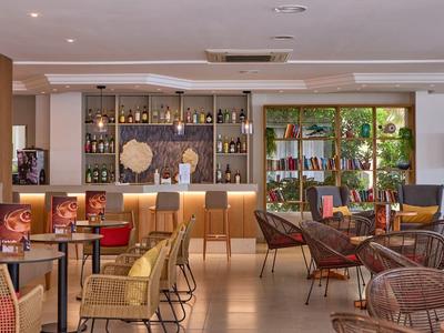 Przytulny bar hotelowy z krzesłami, stolikami i podświetlaną półką pełną butelek.