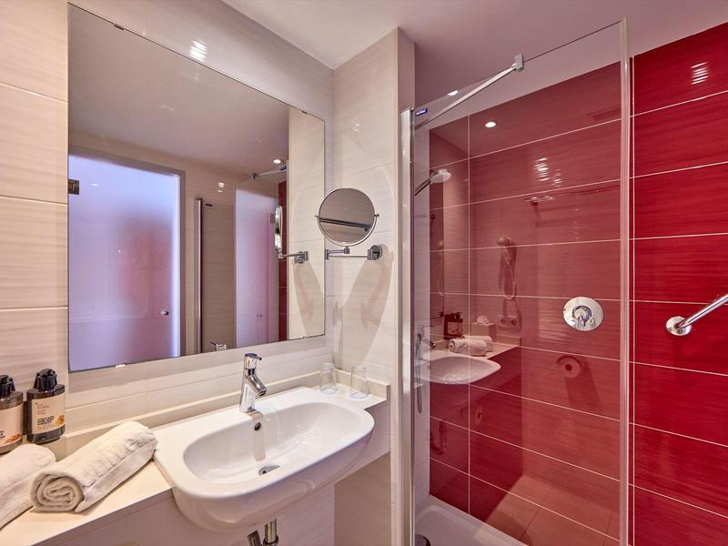 Nowoczesna łazienka z umywalką i szklanymi czerwonymi drzwiami prysznica.