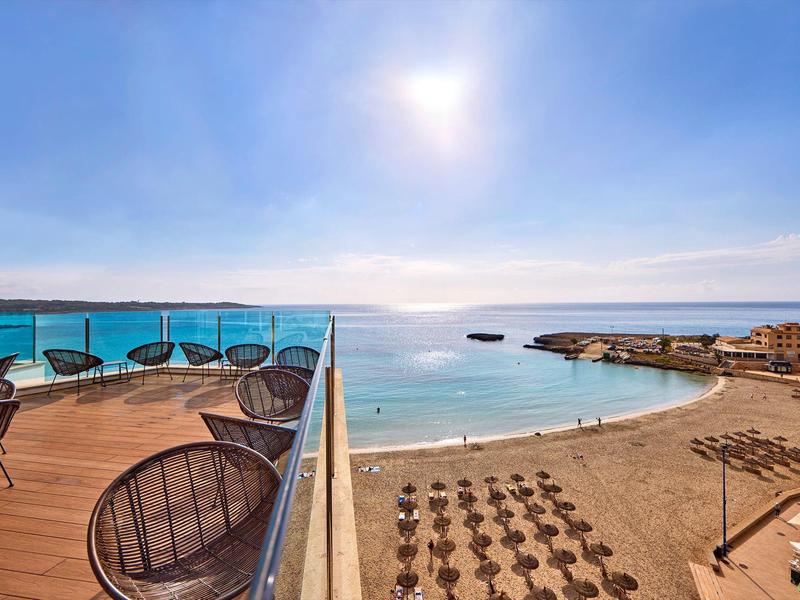 Widok z tarasu z krzesłami na plażę z parasolami i morze pod bezchmurnym niebem.