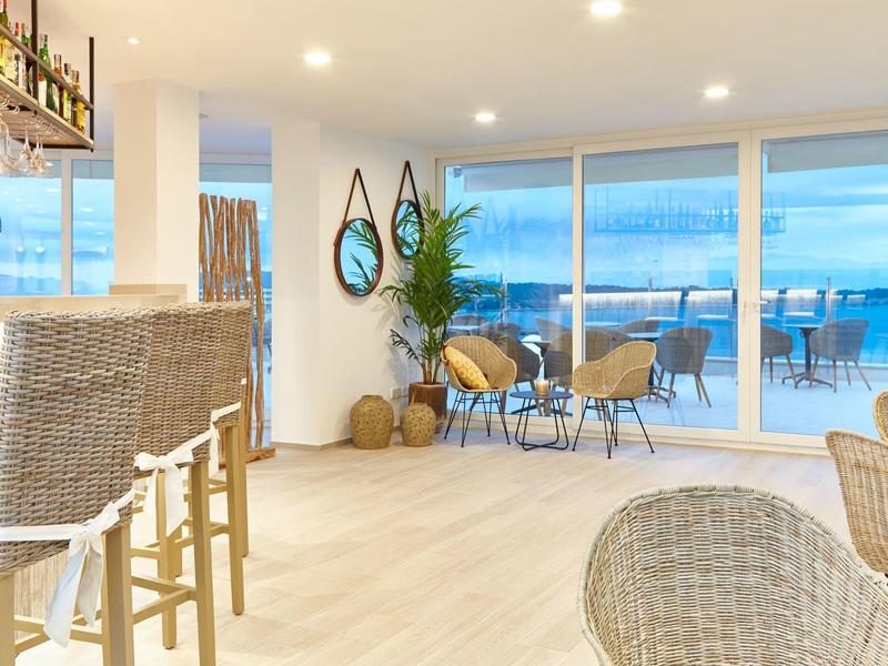 Jasne wnętrze hotelu z barem, strefą wypoczynkową i dużym panoramicznym oknem z widokiem na morze.