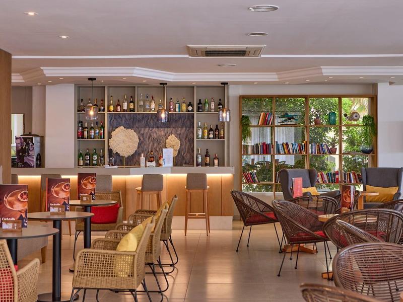 Przytulny bar hotelowy z krzesłami, stolikami i podświetlaną półką pełną butelek.