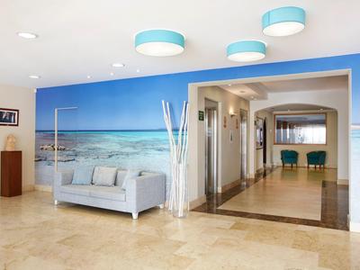 Lichte hotellobby met een strandmuur, een grijze bank en moderne blauwe lampen.