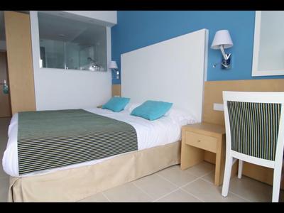 Moderne hotelkamer met groot bed, blauwe kussens, bureau en flatscreen-tv.