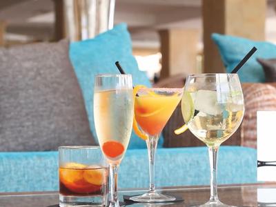 Vier verschillende cocktails op een tafel met blauwe en grijze kussens op de achtergrond.