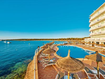 Piscine d'hôtel avec parasols et transats à côté de la mer sous un ciel dégagé.