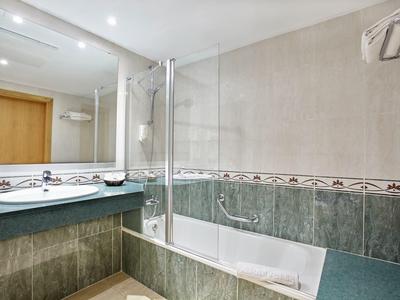 Moderne badkamer met een bad en douche combineren, groene tegels en grote spiegel boven de wastafel.