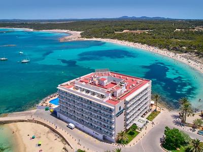Groot strandhotel met rood dak langs turquoise baai en zandstrand