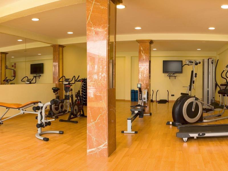 Hotelgym met hometrainers, loopband, roeimachine en gewichten in een ruime kamer.