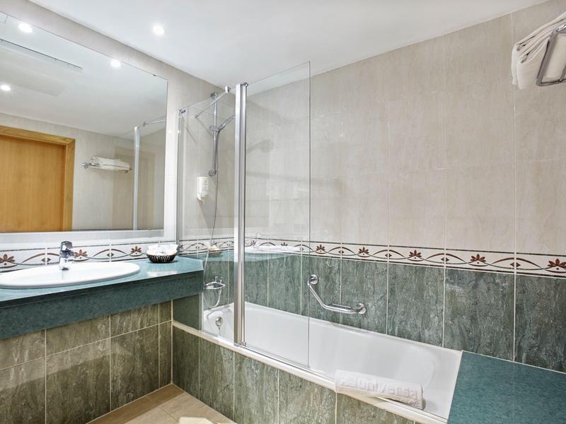 Moderne badkamer met een bad en douche combineren, groene tegels en grote spiegel boven de wastafel.