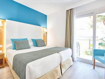 Bright hotel room with twin beds, blue accents, and a balcony with outdoor seating.