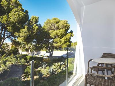 Balcony with wicker chairs overlooking green garden and trees under a clear blue sky.