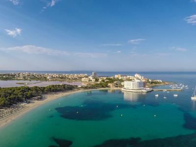Coastal resort with clear turquoise waters, white sandy beach, and buildings under a blue sky.