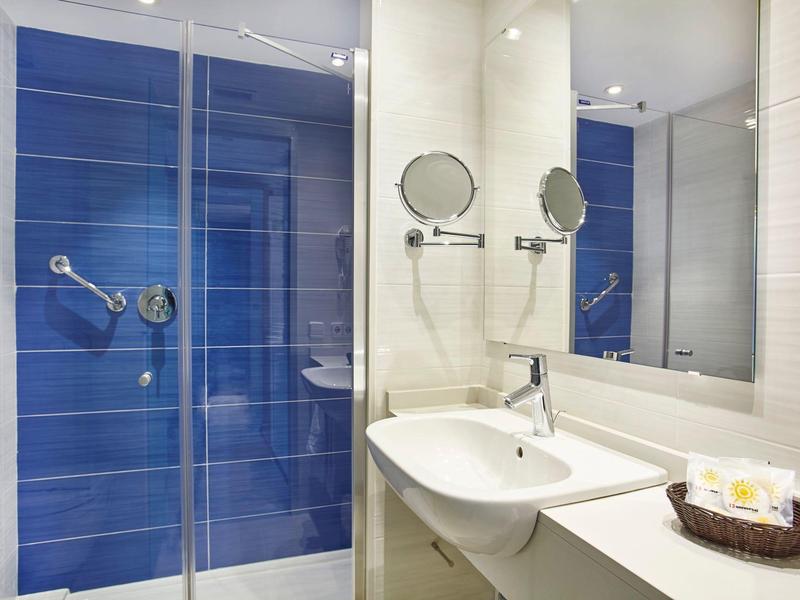 Modern hotel bathroom with blue-tiled shower and white sink countertop.