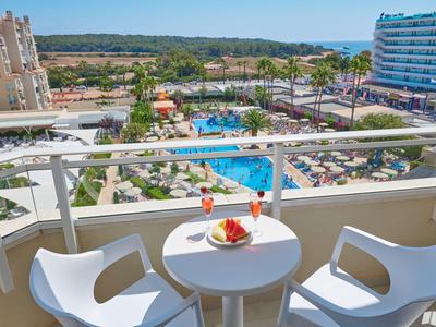 Balcone con vista su piscina, lettini e hotel vicini in una località di vacanza soleggiata.