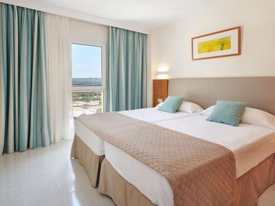 Camera d'hotel luminosa con due letti, tende turchesi e vista sulla piscina.