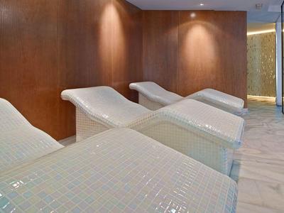 Lettini moderni e rilassanti con piastrelle a mosaico bianche in una stanza benessere.