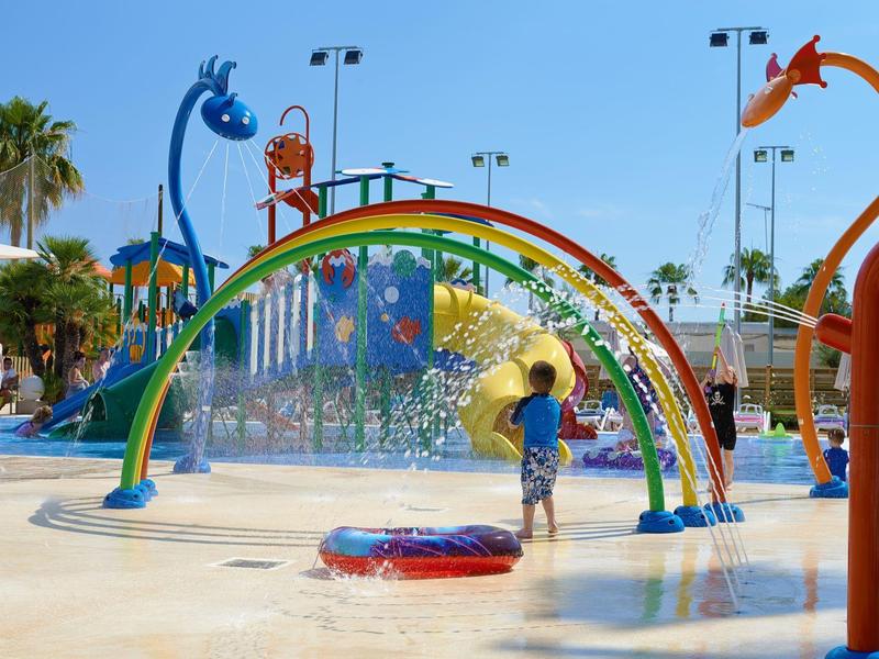 Bambini che giocano in un'area giochi acquatica colorata sotto un cielo azzurro brillante.