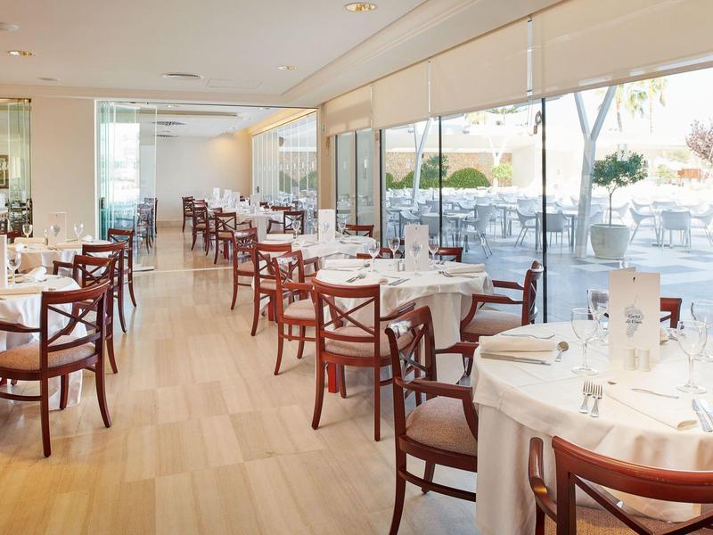 Ristorante dell'hotel luminoso con tovaglie bianche e sedie di legno accanto a una terrazza.