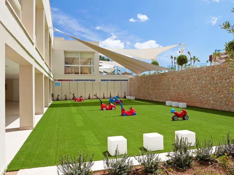 Cortile moderno con prato sintetico e attrezzature da gioco in ambiente alberghiero.