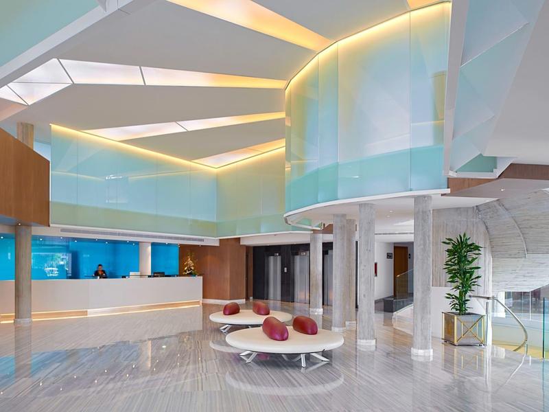 Moderna hall d'hotel con banco reception bianco e divano rotondo sotto grandi soffitti luminosi.