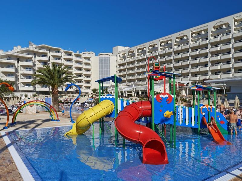 Area giochi acquatica colorata con scivoli davanti a un grande hotel sotto un cielo azzurro.
