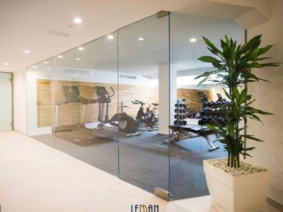 Moderní posilovna za skleněnou stěnou s vybavením a závažími v světlém interiéru.