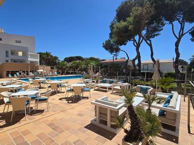 Hotelowy taras z stołami, krzesłami i basenem pod niebieskim niebem i drzewami.