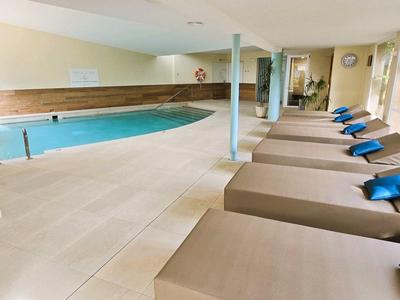 Wnętrze z basenem i leżakami z niebieskimi poduszkami w jasnej strefie spa.