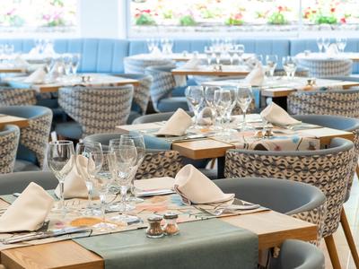 Elegancka restauracja z nakrytymi stołami i plecionymi krzesłami, jasna atmosfera.