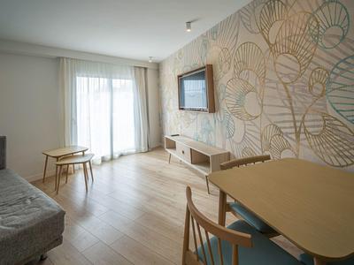 Jasny salon z sofą, stolikiem kawowym, jadalnią i dużym oknem z zasłonami.