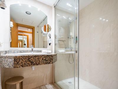 Jasna łazienka hotelowa z granitową umywalką, szklaną prysznicem i stołkiem.