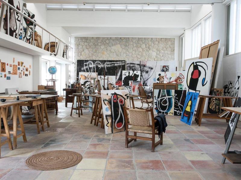 Jasne atelier z krzesłami malarskimi, sztalugami i nowoczesnymi dziełami sztuki w przestronnym pomieszczeniu.