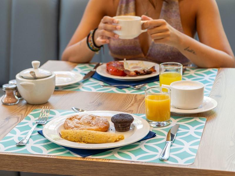Stół śniadaniowy z bajglem, sokiem, kawą i osobą trzymającą filiżankę.