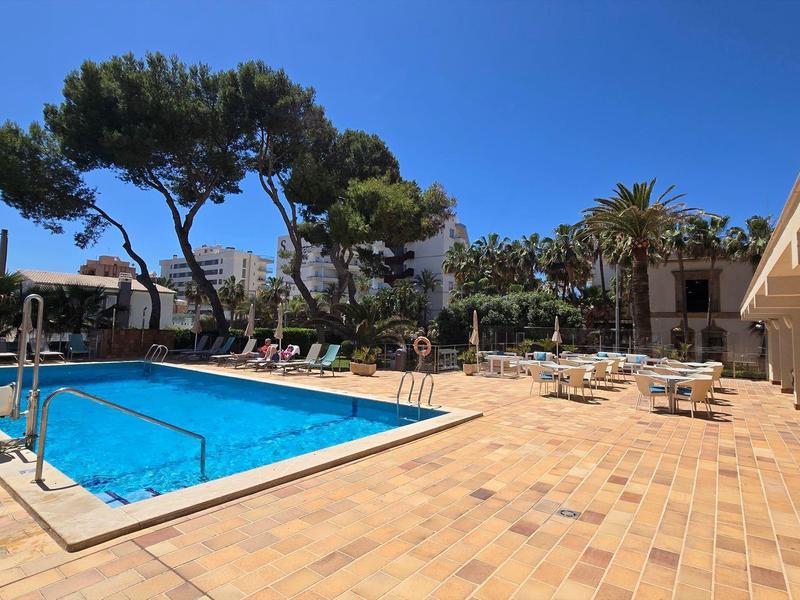 Duży basen hotelowy z niebieską wodą, otoczony leżakami i drzewami.